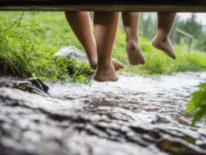 dei piedi di bambini penzolano fa un pontile su di un ruscello