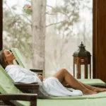 una donna sdraiata su una poltrona relax dietro ampie finestre da cui si intravedono alberi e vegetazione